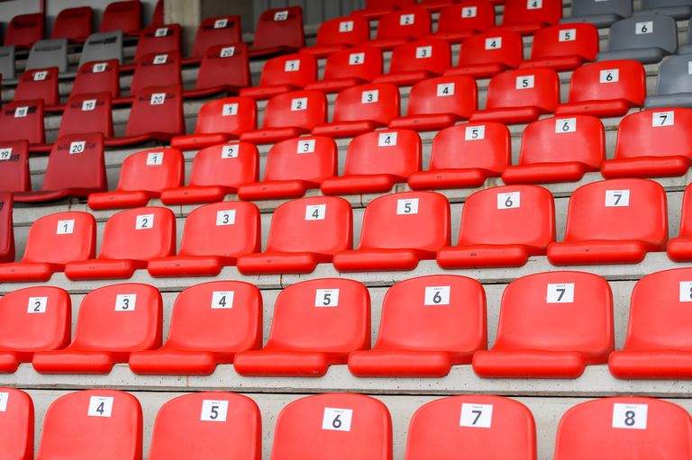 Eine Reihe roter Sitze, nummeriert von 1 bis 7, in einem Stadion angeordnet mit leeren Plätzen.