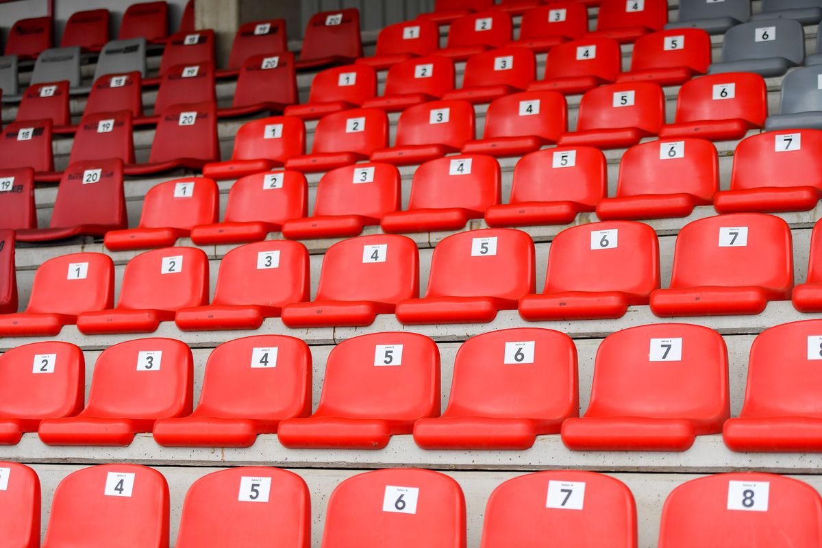 Eine Reihe roter Sitze, nummeriert von 1 bis 7, in einem Stadion angeordnet mit leeren Plätzen.