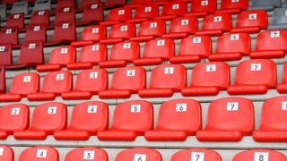 Eine Reihe roter Sitze, nummeriert von 1 bis 7, in einem Stadion angeordnet mit leeren Plätzen.
