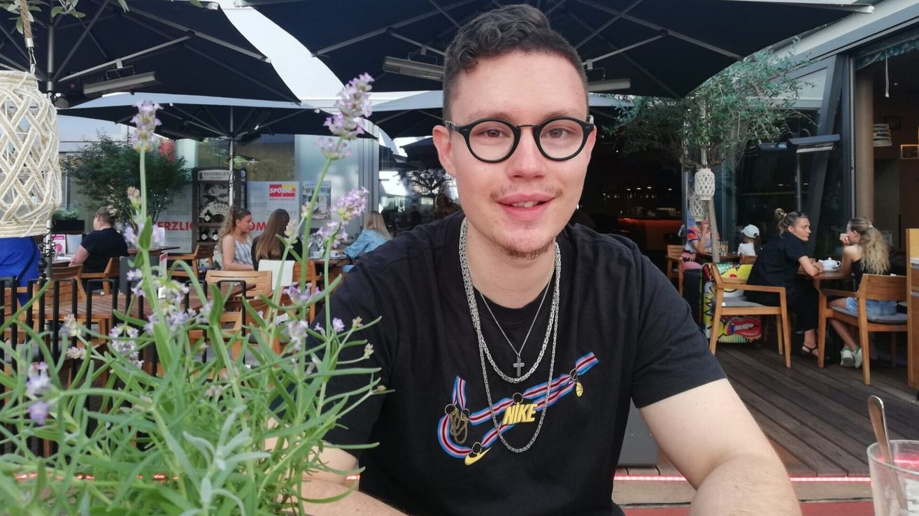 Ein Mann mit Brille und einem schwarzen T-Shirt mit Nike-Logo sitzt draußen in einem Restaurant.