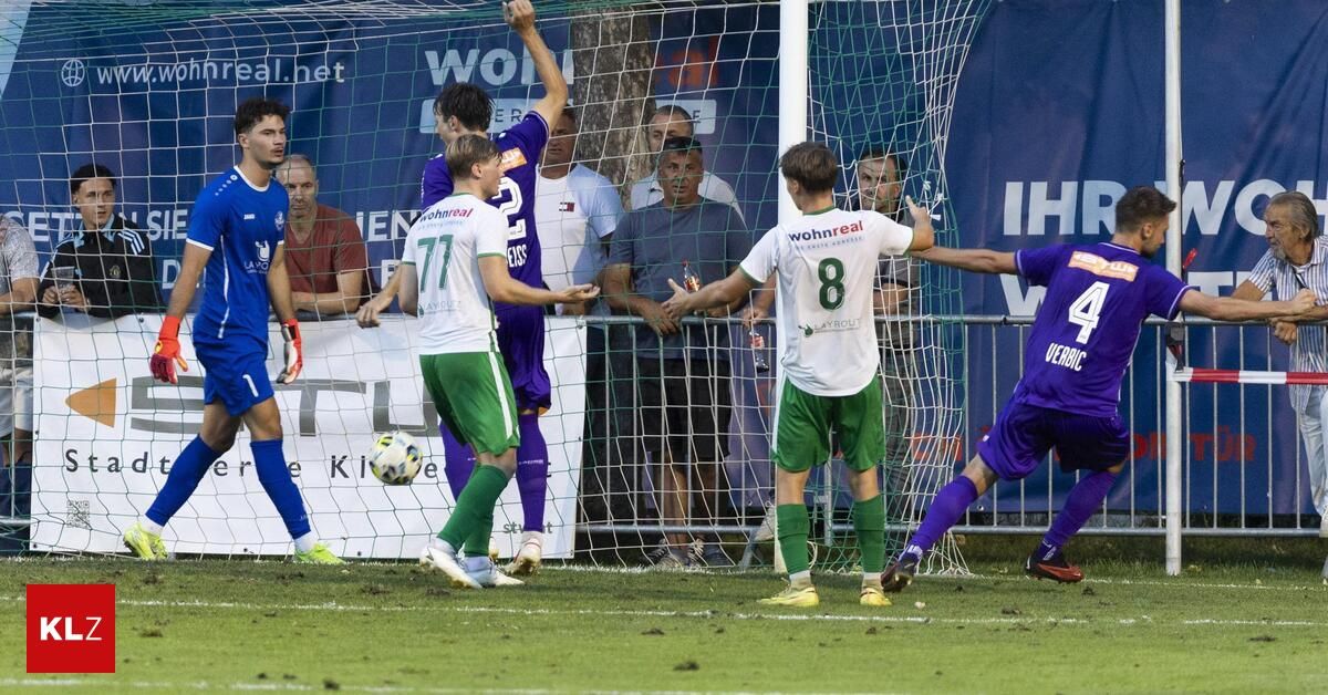 Fußballspieler feiern ein Tor vor einem Tornetz, während Zuschauer hinter einem Zaun zuschauen.