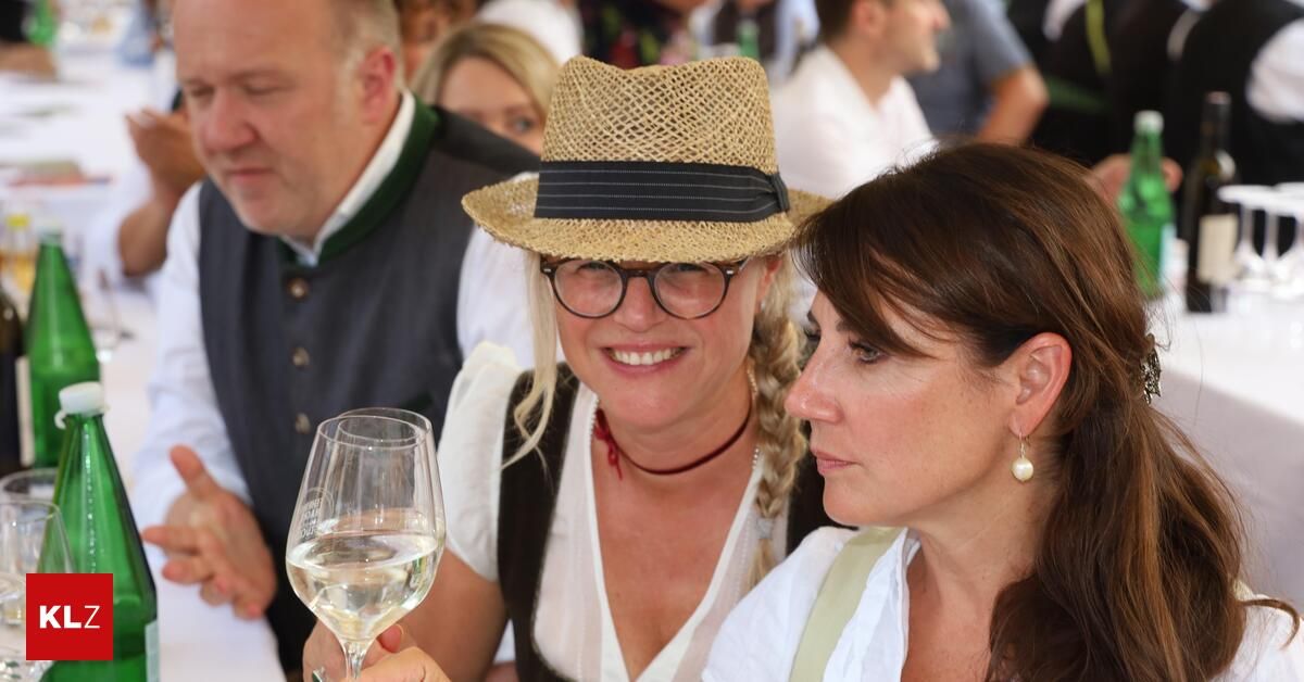 Zwei Frauen bei einem gesellschaftlichen Treffen, eine mit Strohhut und Weinglas, die andere mit geflochtenen Haaren und Ohrringen.