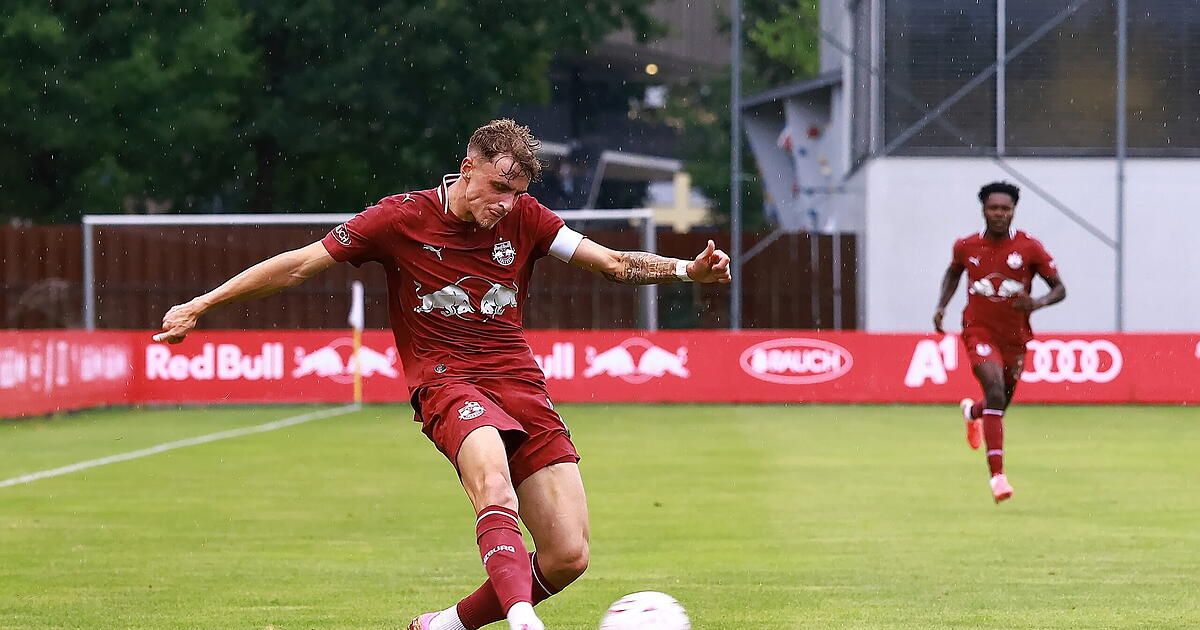 Ein Fußballspieler in einem roten Trikot tritt einen Ball auf einem nassen Feld.