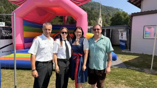 Vier Personen stehen vor einem großen, bunten aufblasbaren Schloss mit einem Berg und einer Kirche im Hintergrund.