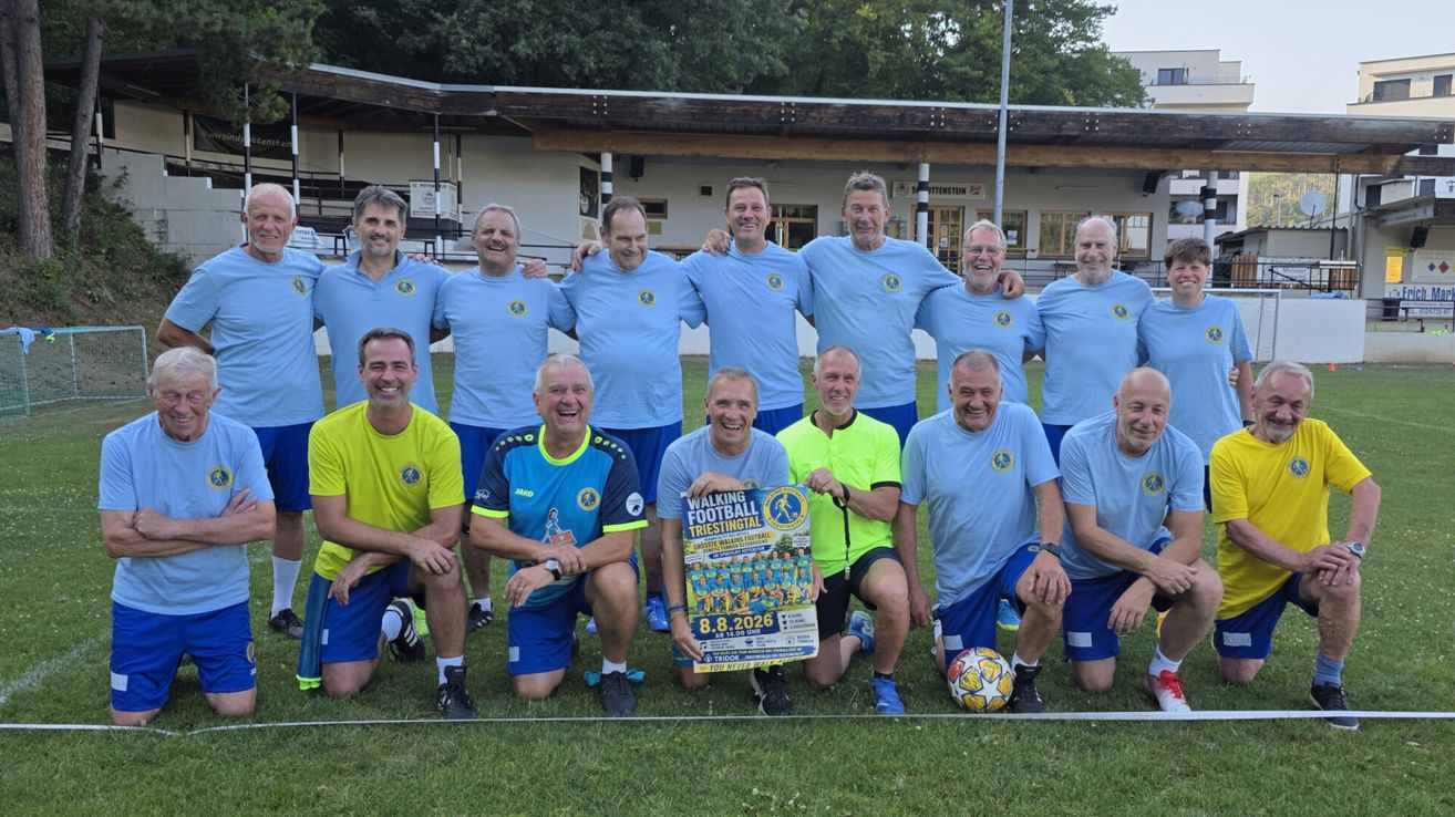 Eine Gruppe von Männern in blauen und gelben Uniformen posiert für ein Foto auf einem Fußballfeld mit einem Schild, das 'Walking Football Triestringtal' besagt.