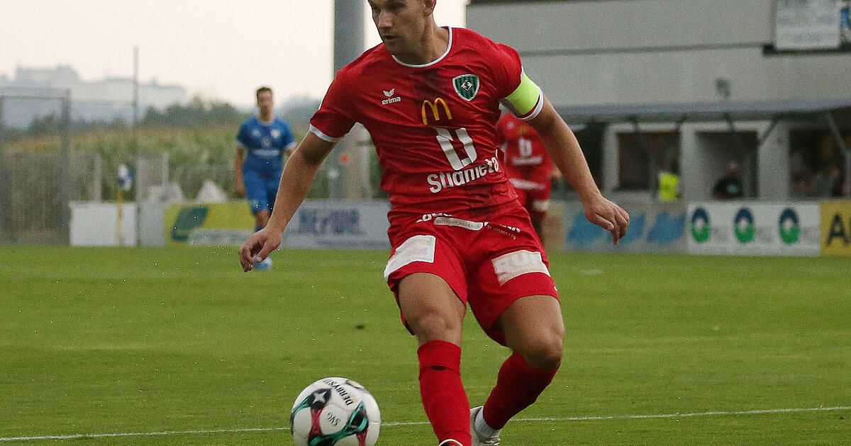 A soccer player in a red uniform with the number 11 on the back is running and kicking a soccer ball on a field.