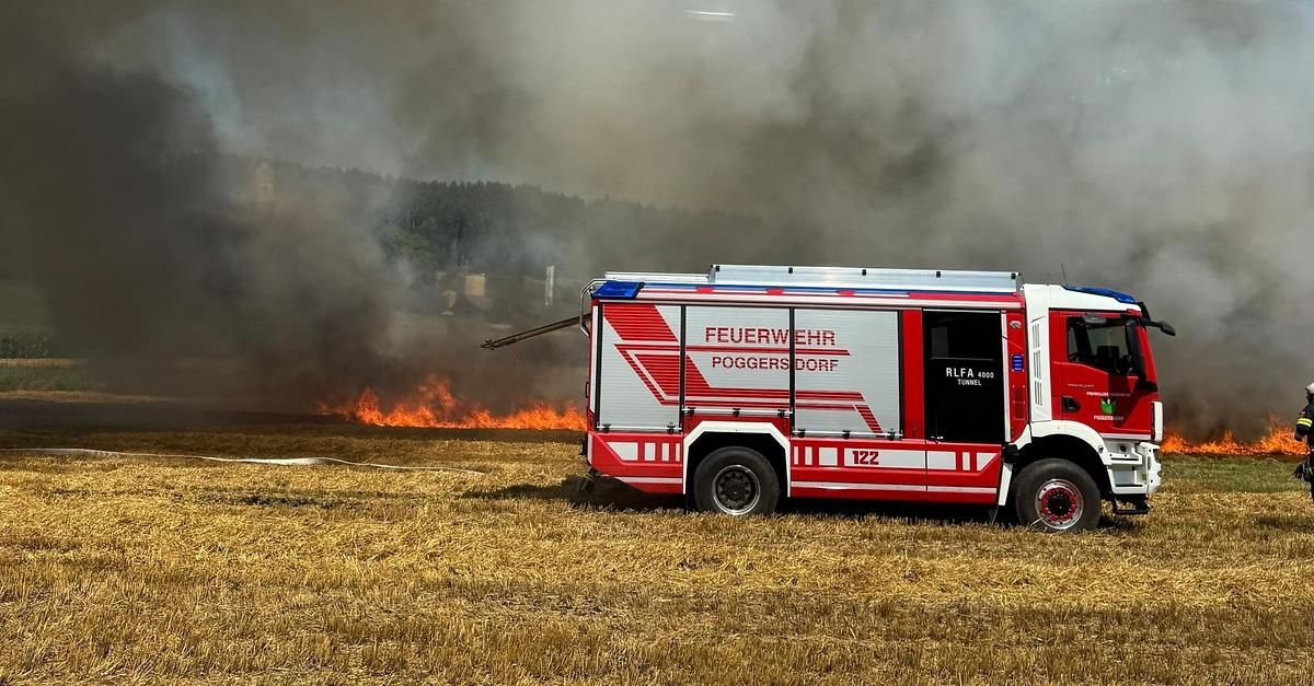 Ein rot-weißer Feuerwehrwagen mit der Aufschrift 'Feuerwehr Poggers Dorf' steht auf einem Feld, mit einem Feuer im Hintergrund.