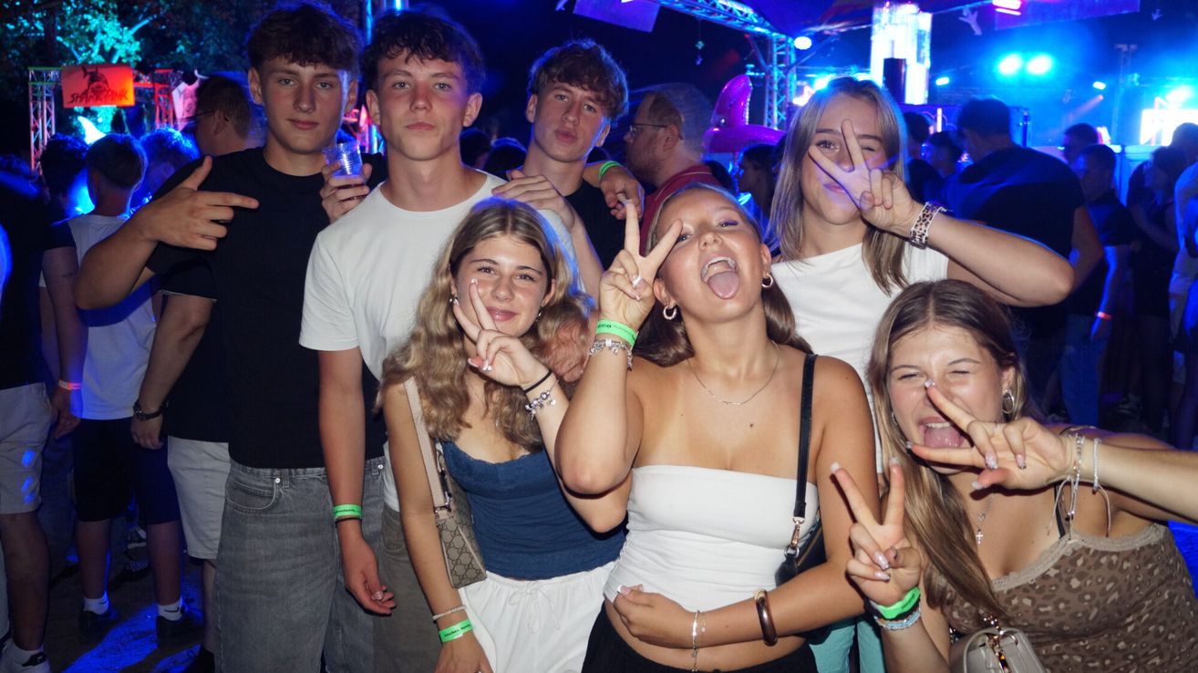 Eine Gruppe junger Leute posiert für ein Foto in einem Nachtclub, einige machen Friedenszeichen und andere lächeln.
