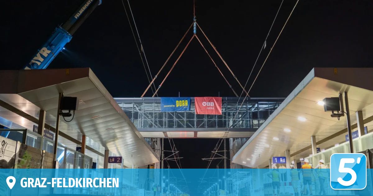 Eine nächtliche Baustelle an einem Bahnhof mit einer neu installierten Brücke, gekennzeichnet durch Banner und Arbeiter in Sicherheitsausrüstung.