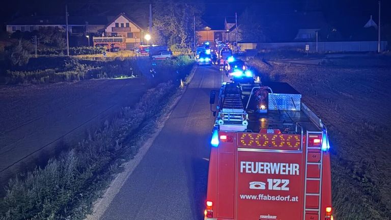 A fire truck with its lights on is driving down a road with other emergency vehicles, likely responding to an incident in a rural area at night.