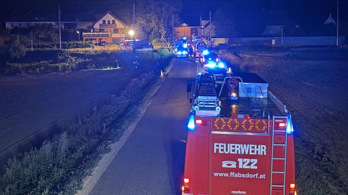 A fire truck with its lights on is driving down a road with other emergency vehicles, likely responding to an incident in a rural area at night.