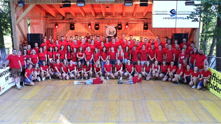 Eine Gruppe von Menschen in roten T-Shirts posiert für ein Foto in einem Raum mit Holzwänden und einem Banner, das 'Verti Blech' steht.