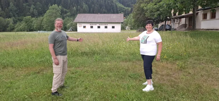Ein Mann und eine Frau stehen auf einer Wiese mit einem Haus namens Reitstall Schiestlhof im Hintergrund.