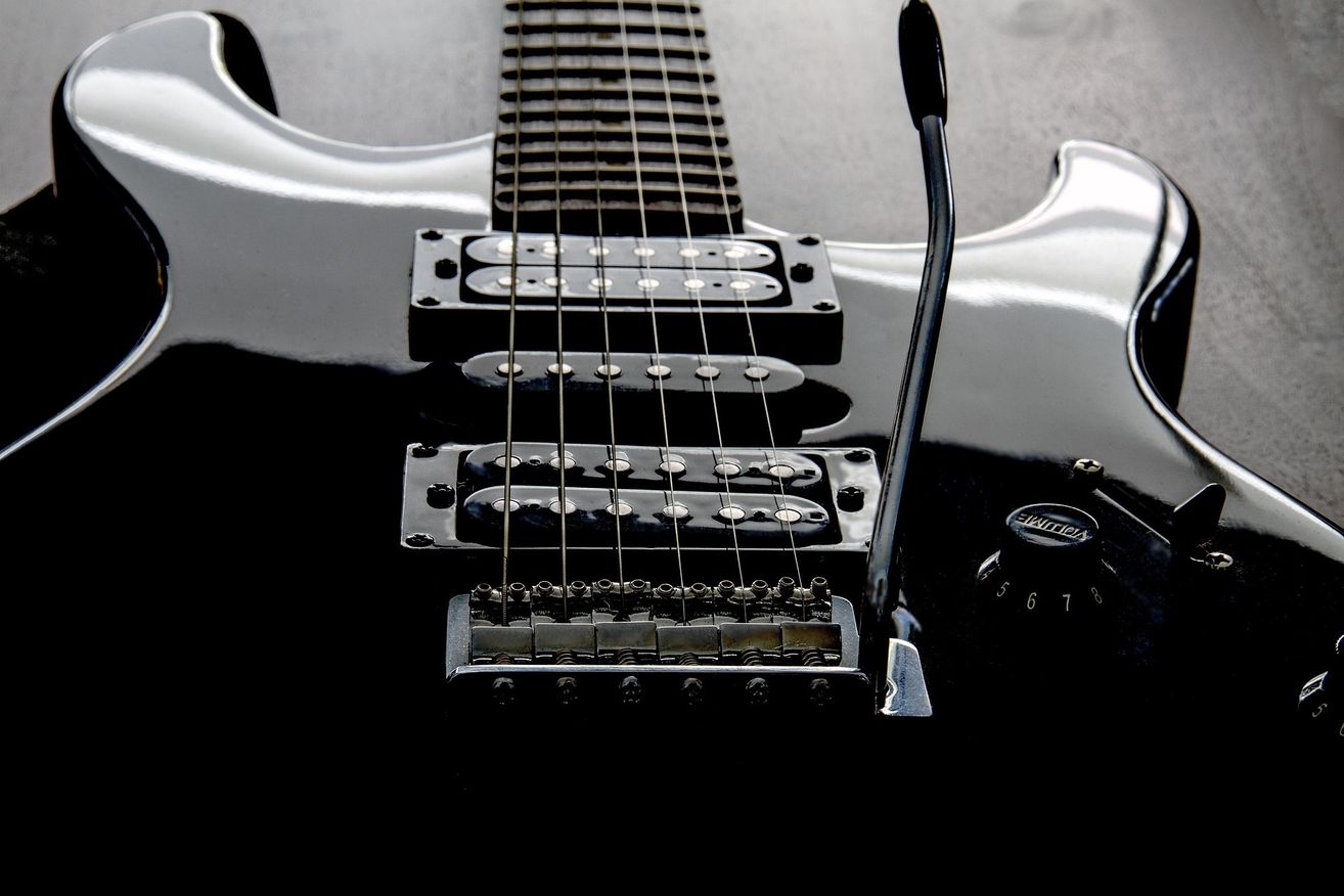 Nahaufnahme einer schwarzen E-Gitarre mit mehreren Tonabnehmern und angeschlossenem Mikrofon. Die Gitarre hat einen glänzenden Finish und aufwendige Metalldetails.
