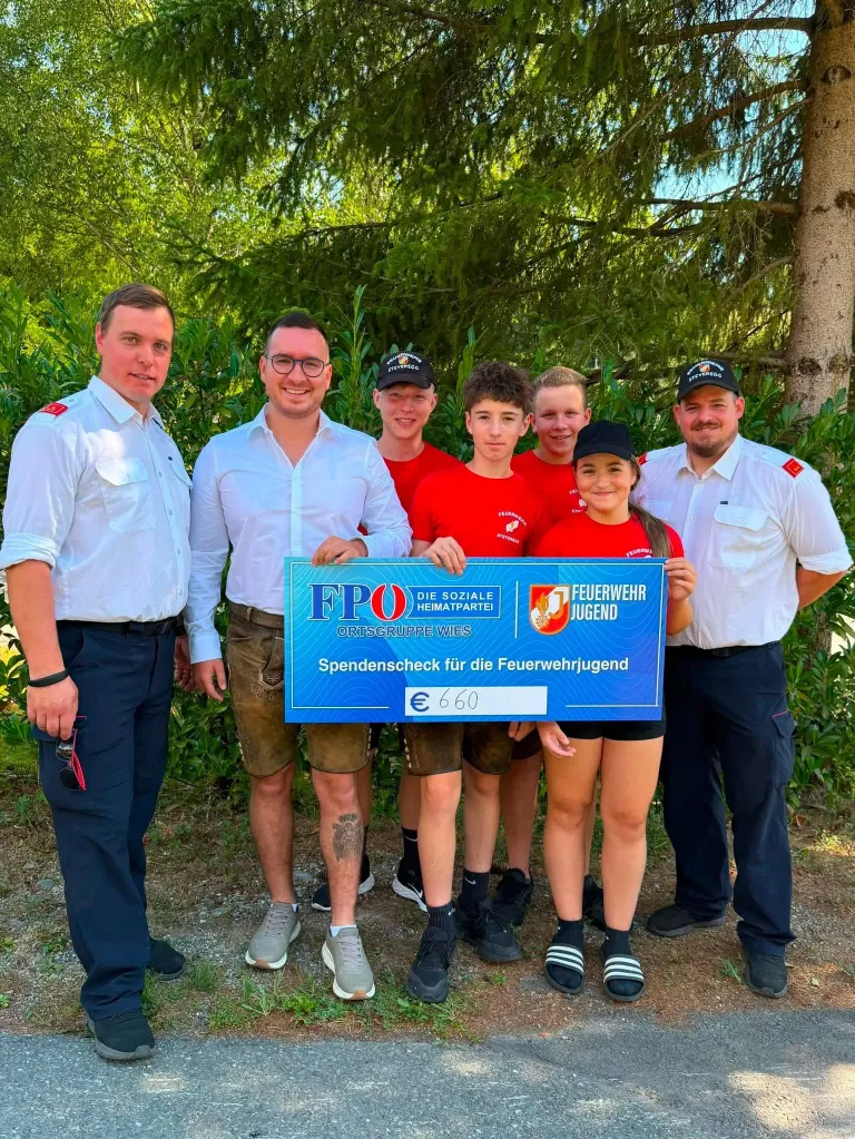 A group of firefighters and young people are posing for a photo with a donation check for 660 euros. The check is held by a young girl.
