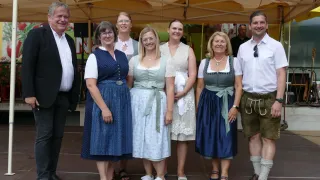 Eine Gruppe von Menschen in traditioneller deutscher Kleidung posiert für ein Foto unter einem Zelt. Sie lächeln und scheinen auf einem Festival zu sein.