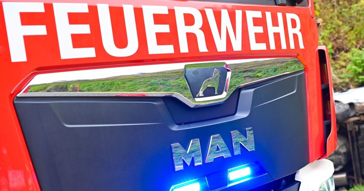 Eine Nahaufnahme der Vorderseite eines blauen und roten Fahrzeugs mit den Worten MAN und FEUERWEHR in weißen Buchstaben. Das Fahrzeug hat ein Wolfslogo und blaue Lichter.