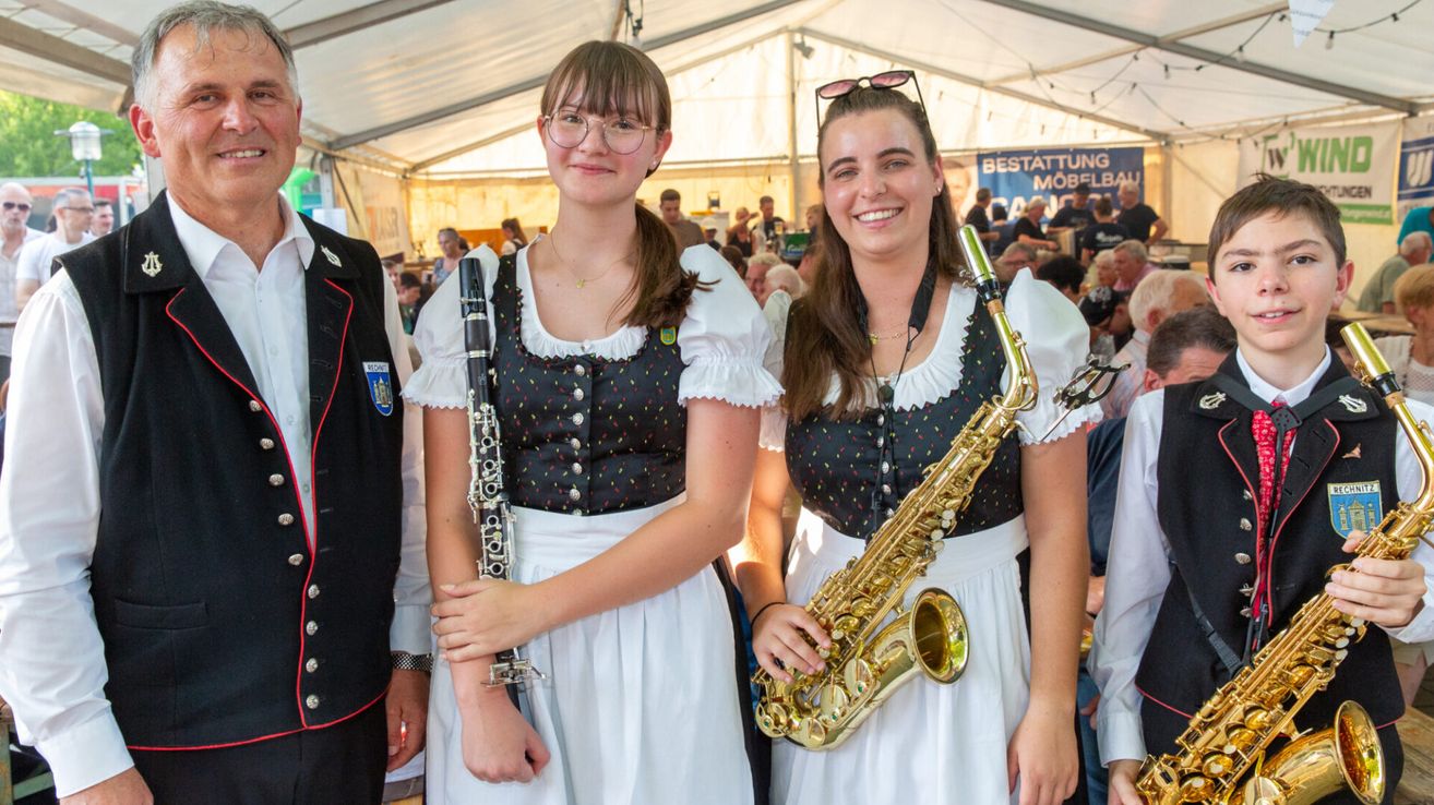 Zwei Frauen in traditioneller deutscher Kleidung, eine mit einer Klarinette und die andere mit einem Saxophon, lächeln und posieren für ein Foto bei einer Veranstaltung im Freien.