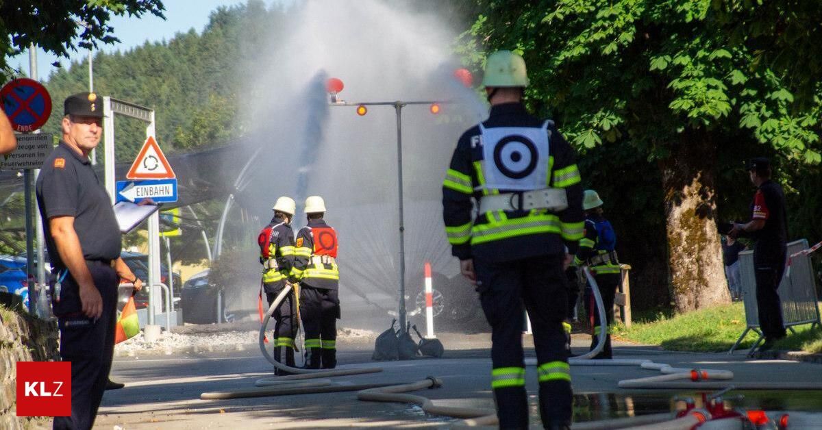 Feuerwehrleute verwenden einen Schlauch, um ein Feuer auf einer Straße zu löschen, wobei Rauch und Wasser um sie herum sprühen.