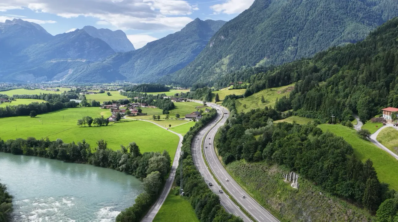 Luftaufnahme einer kurvenreichen Straße durch ein üppiges grünes Tal mit Bergen im Hintergrund.