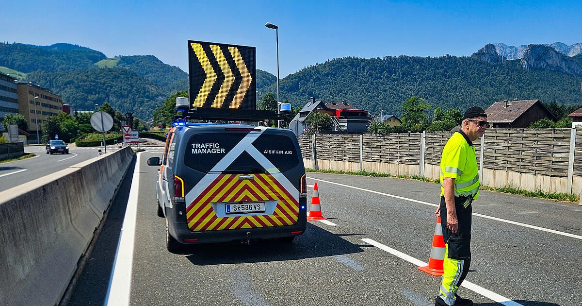 Ein Van eines Verkehrsmanagers mit blinkendem Schild ist am Straßenrand eines Highways geparkt, mit orangefarbenen Verkehrskegel. Ein Mann in einer reflektierenden Weste steht in der Nähe.