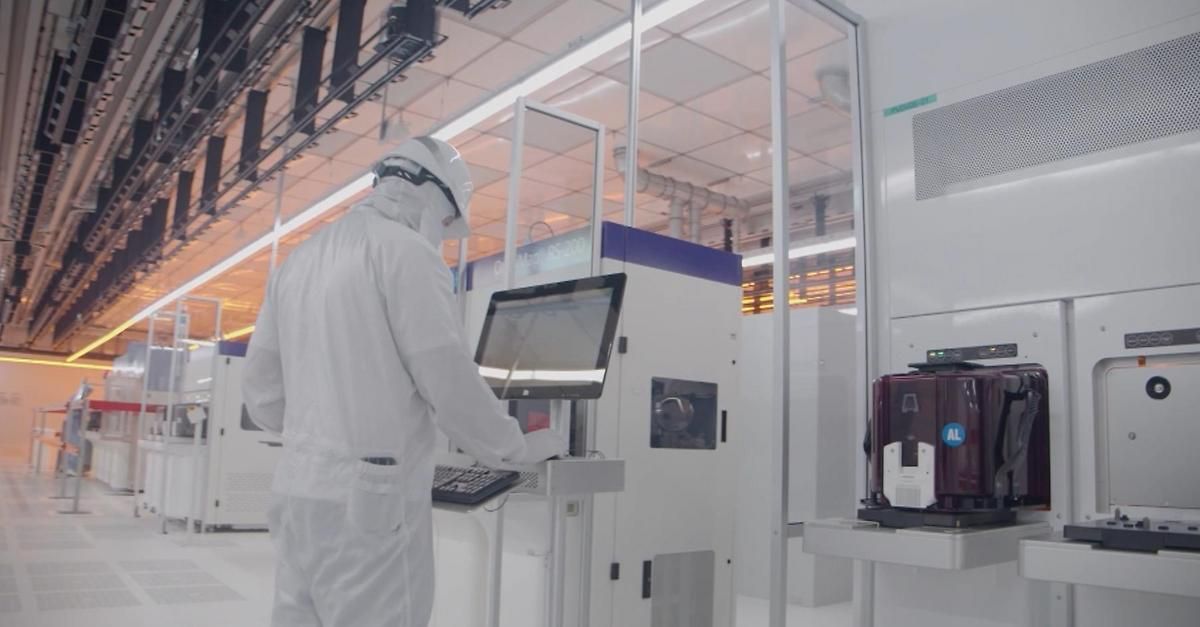 Eine Person in einem weißen Laborkittel und Schutzausrüstung arbeitet an einem Computer in einer High-Tech-Fabrik.