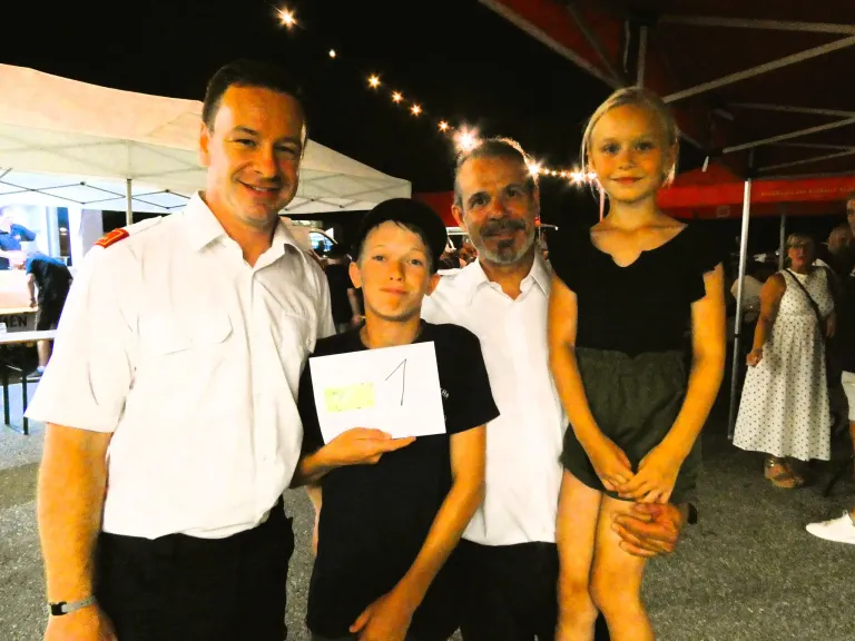 Drei Erwachsene und zwei Kinder stehen nachts unter einem Zelt und lächeln für ein Foto. Der Junge hält ein Stück Papier mit der Nummer eins.