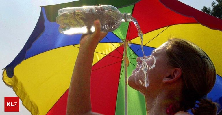 A woman drinks water from a bottle under a colorful umbrella on a sunny day.