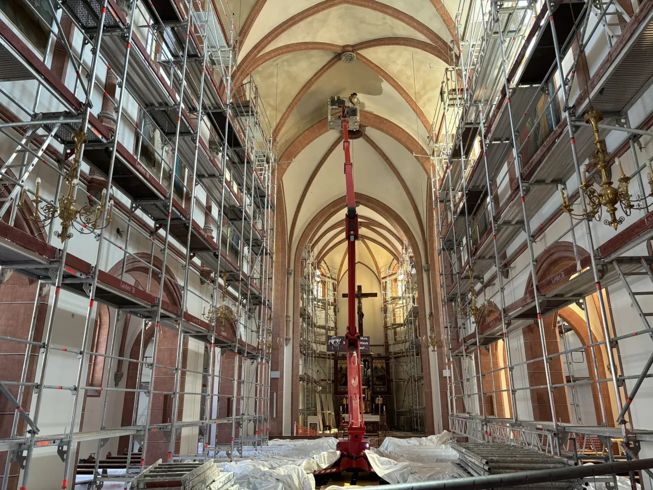Eine Person auf einem roten Scherenarbeitsbühne in der Mitte einer Kirche in Renovierung, umgeben von Gerüsten.