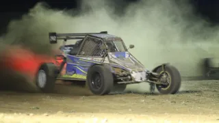 Ein blaues und gelbes Offroad-Fahrzeug fährt auf einer unbefestigten Strecke und wirbelt Staub und Rauch auf.
