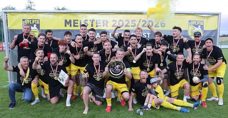 A soccer team celebrates their victory with medals and a trophy. The team is wearing black and yellow uniforms. The background features a yellow banner with the text 'MEISTER 2025/2026'.