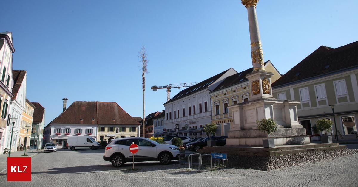 Ein weißer Wagen ist vor einem Denkmal mit einem roten und weißen Schild auf einer Kopfsteinpflasterstraße geparkt. Hinter dem Auto befindet sich ein Gebäude mit einem Kran auf dem Dach.