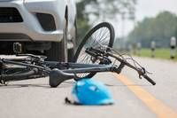 Ein Fahrrad liegt auf der Straße mit einem blauen Helm in der Nähe, und ein Auto ist dahinter geparkt.