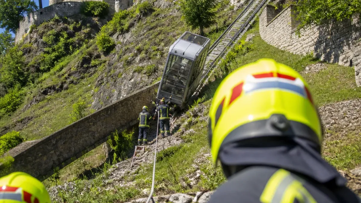Feuerwehrleute in gelben Helmen sichern eine entgleiste Seilbahn auf einem steilen Bergpfad.