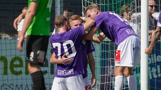 Drei Fußballspieler in lila Trikots feiern ein Tor vor einem grünen Netz. Der Spieler in der Mitte trägt die Nummer 70.