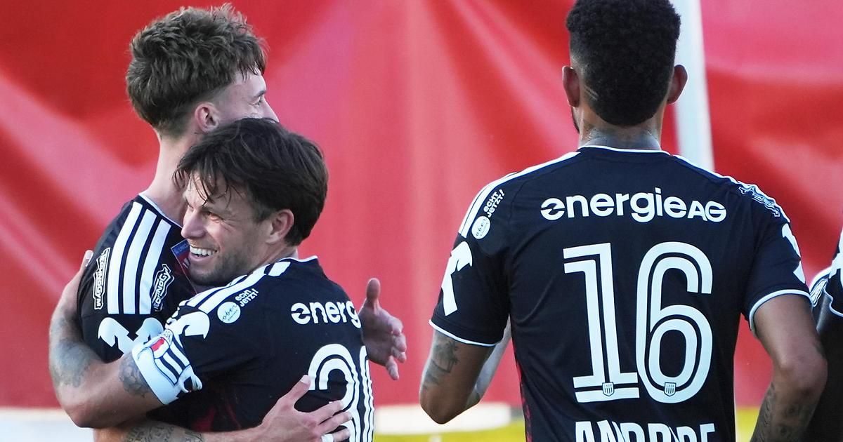 Drei Fußballspieler feiern ein Tor, einer trägt ein Trikot mit der Nummer 3 und ein anderer die Nummer 16. Der Spieler in der Mitte lächelt und umarmt den Spieler auf seiner linken Seite.