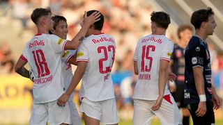 Vier Fußballspieler in weißen Trikots mit roten Akzenten feiern ein Tor. Der Spieler in der Mitte hat die Nummer 22 auf dem Rücken.