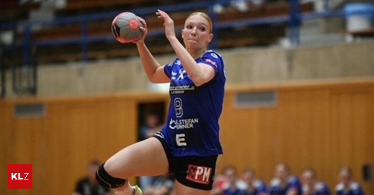Eine Handballspielerin in einem blauen Trikot mit der Nummer 9, in der Luft, bereit, den Ball zu werfen. Der Hintergrund zeigt ein verschwommenes Publikum und eine Holzwand.