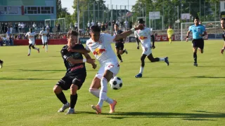 Zwei Fußballspieler kämpfen auf einem Feld um den Ball, während eine Menge im Hintergrund zusieht.