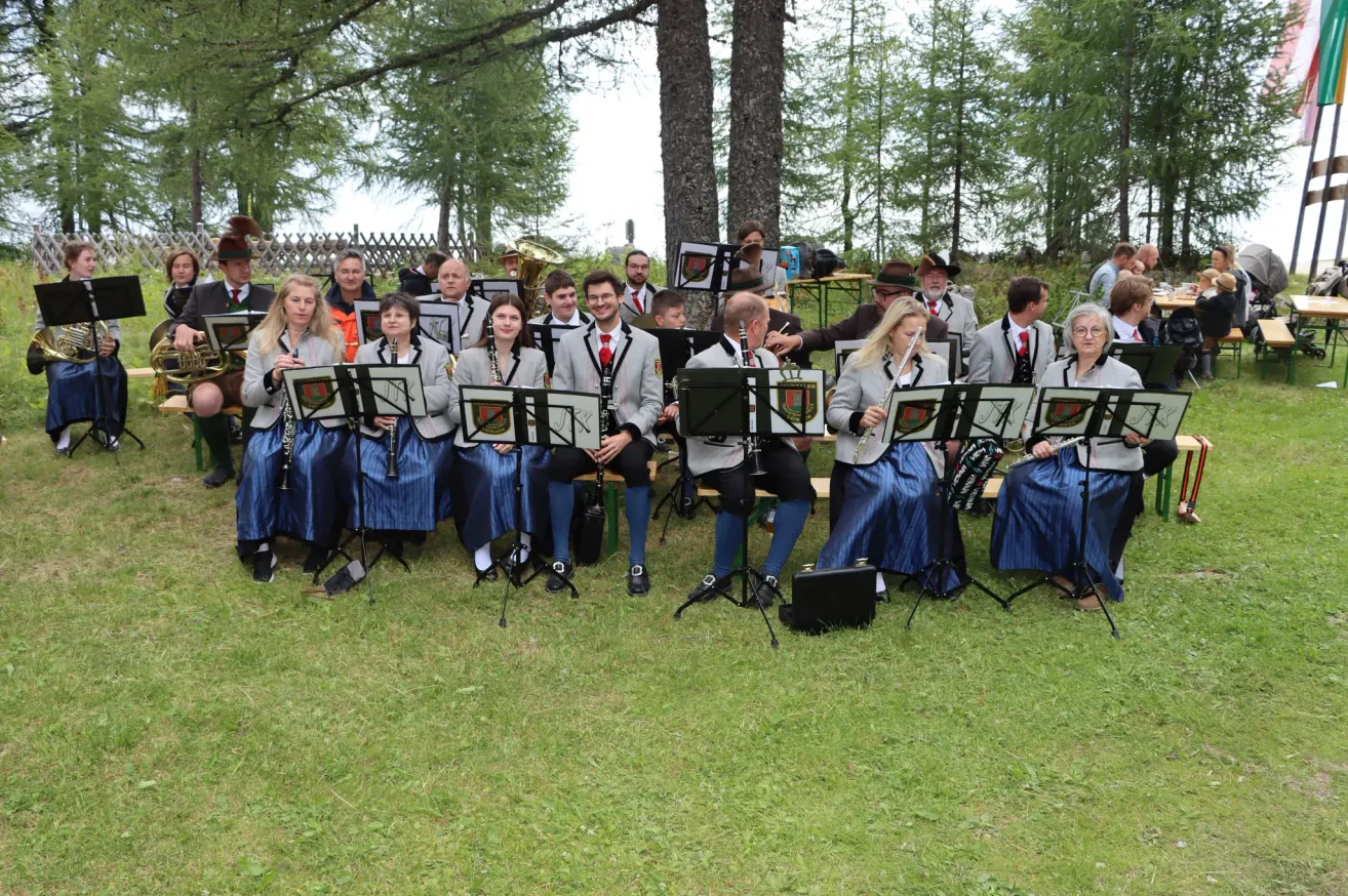 Eine Gruppe von Musikern in traditioneller Kleidung, die auf Bänken sitzen und verschiedene Instrumente in einer Außenumgebung spielen.