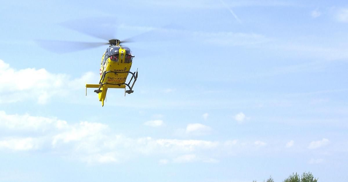Ein gelber Hubschrauber mit der Registrierung OE-XLA fliegt in einem klaren blauen Himmel mit verstreuten Wolken.