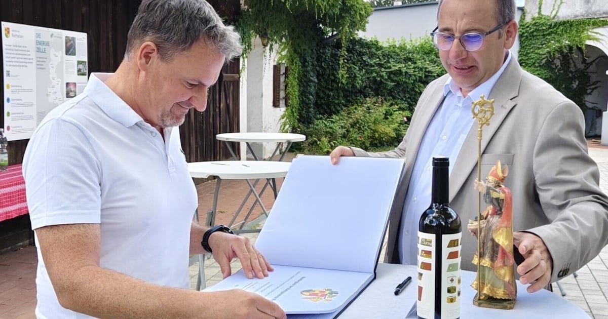 Zwei Männer in formeller Kleidung stehen draußen, einer hält ein offenes Buch und der andere eine Flasche Wein. Sie lächeln und scheinen ein Dokument zu unterzeichnen.