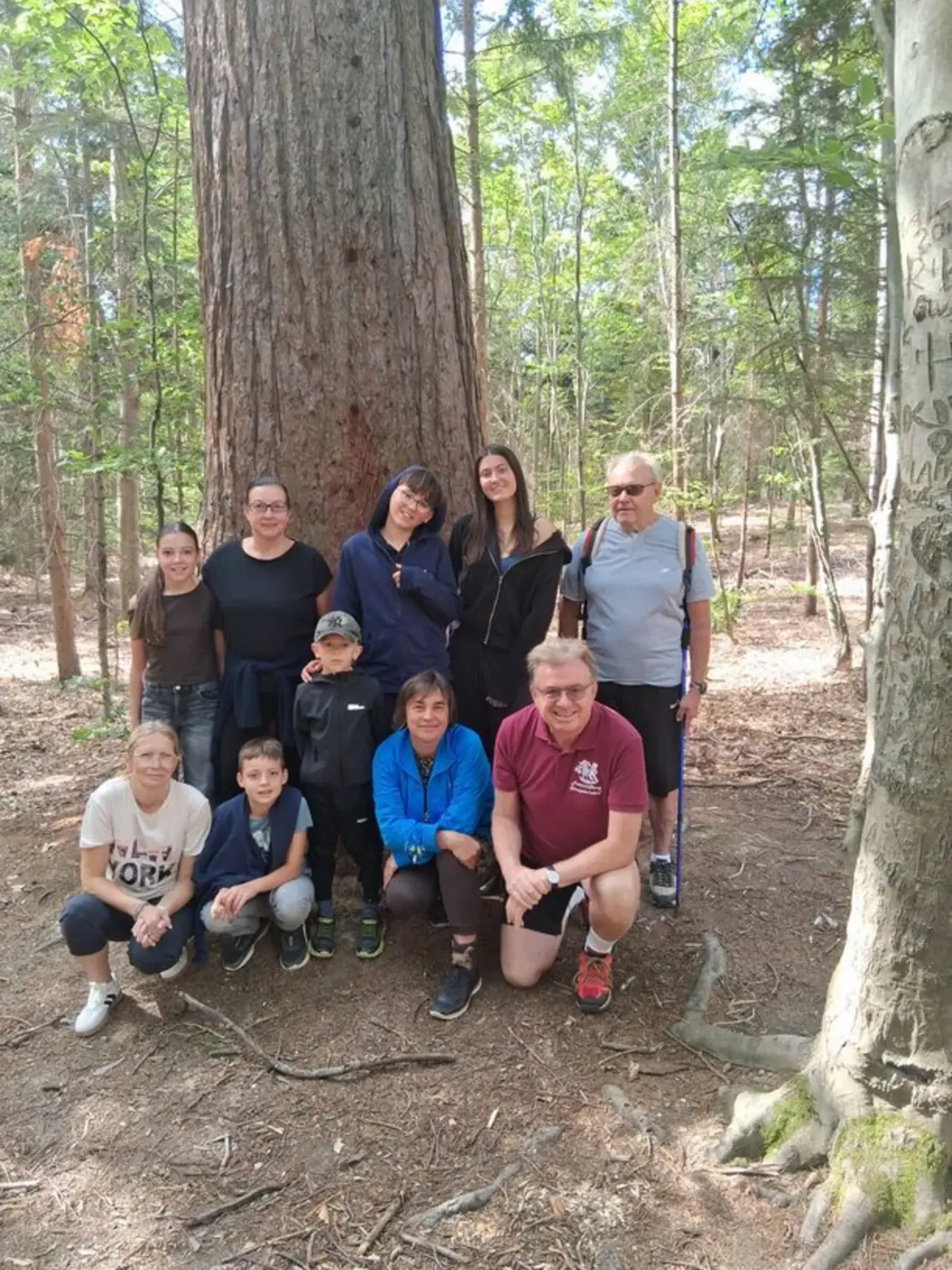 Eine Gruppe von Menschen, einschließlich Erwachsener und Kindern, posiert für ein Foto in einem Wald mit einem großen Baum im Hintergrund.