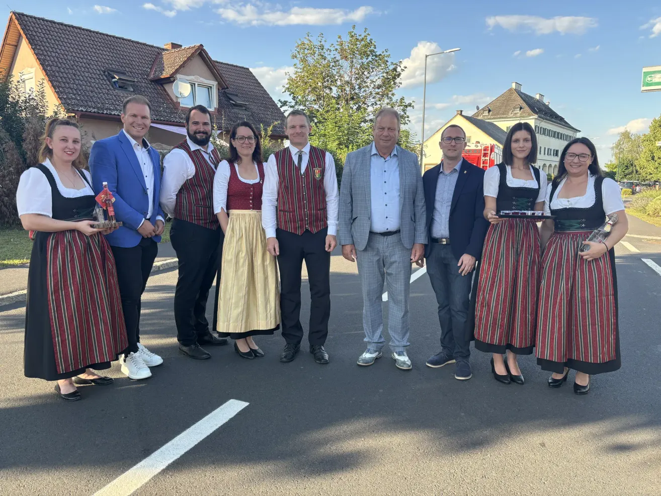 Eine Gruppe von Menschen in traditioneller Kleidung und Business-Anzügen steht auf einem Parkplatz und lächelt für ein Foto.