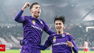 Zwei Fußballspieler in lila Trikots feiern ein Tor, einer mit erhobener Faust und der andere lächelt mit offenem Mund.