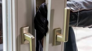 Ein Nahaufnahme einer Türgriffs mit einem schwarzen Handschuh, der ihn teilweise bedeckt, was darauf hindeutet, dass jemand versucht, die Tür zu öffnen.