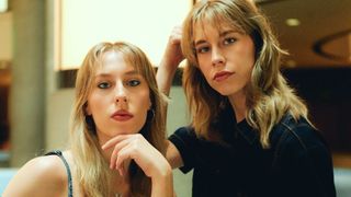 Zwei Frauen mit blonden Haaren, eine in einer Jeansjacke, posieren für ein Foto. Die Frau auf der linken Seite berührt ihr Kinn mit der Hand.