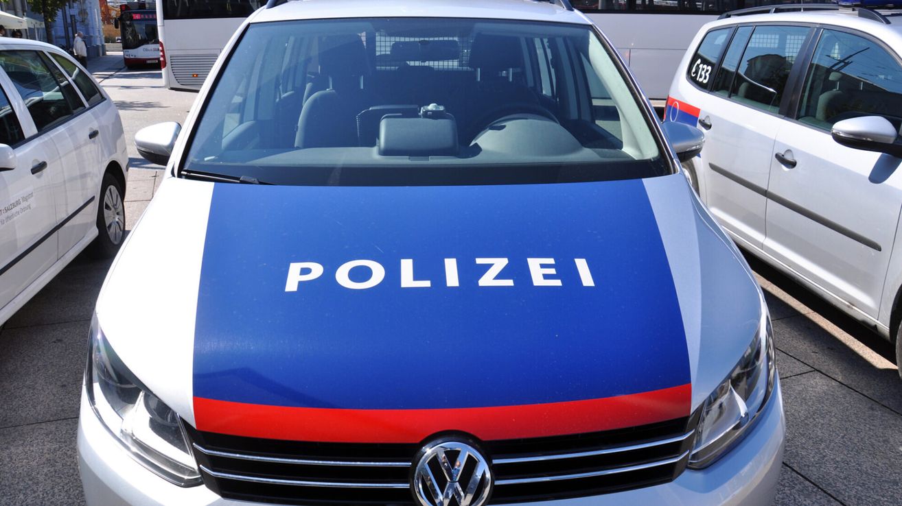 Nahaufnahme der Front eines Polizeifahrzeugs mit dem Wort 'POLIZEI' in Weiß auf blauem Hintergrund, darunter ein roter Streifen.