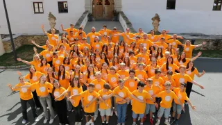 Eine große Gruppe junger Menschen in passenden orangefarbenen T-Shirts posiert für ein Foto vor einem Gebäude.