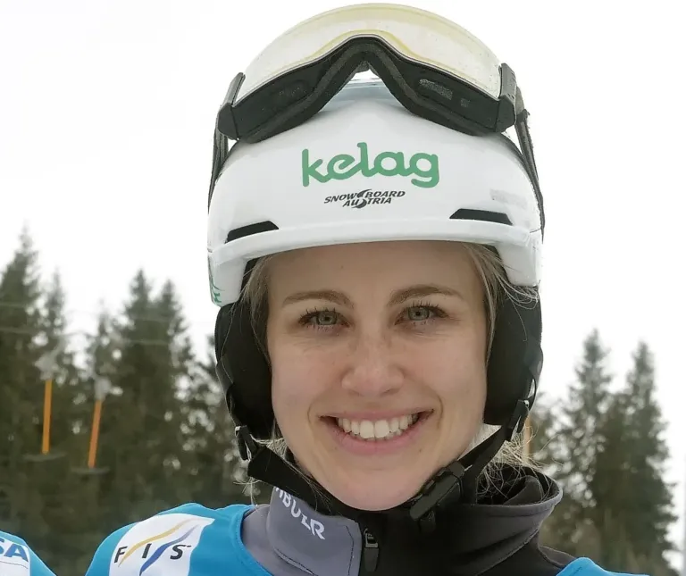 Eine lächelnde Frau mit einem weißen Helm, auf dem das Wort 'kelag' steht, und einer blau-schwarzen Jacke mit FIS auf der linken Seite.
